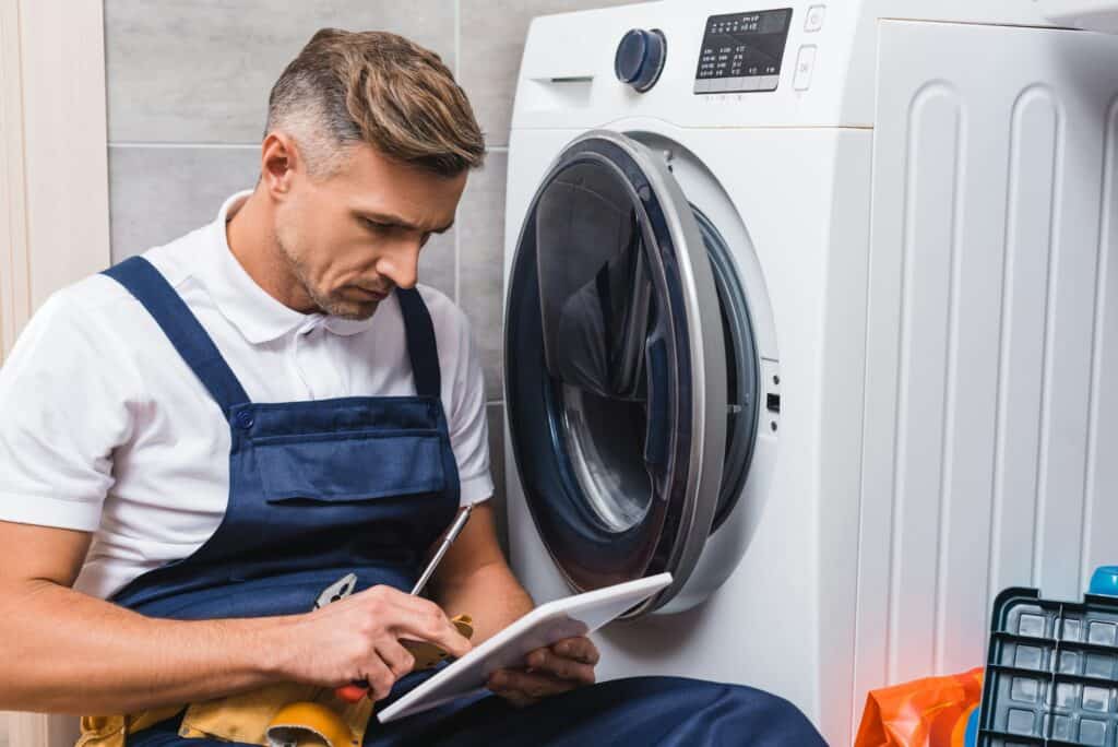 adult repairman holding screwdriver and using digital tablet while repairing washing machine in